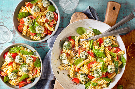 Make this colourful Caprese pasta salad for a fresh summer lunch. Creamy balls of garlic & herbs cheese are rolled in basil and lemon zest, then tossed through pasta with spinach, tomatoes and an easy olive oil dressing for a quick 30 min meal.