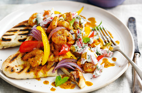 Richly spiced prawns are matched with a creamy, refreshing raita and piled on top of grilled naan bread in this Indian-inspired midweek meal, on the table in less than half an hour.